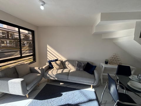 Modern living room with gray sofa, striped pillows, black accents, desk area, and large window with city view