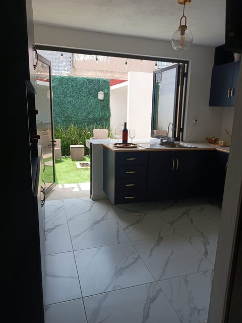 Modern kitchen with black cabinetry, marble flooring, and open glass doors leading to a courtyard with green lawn and hedges