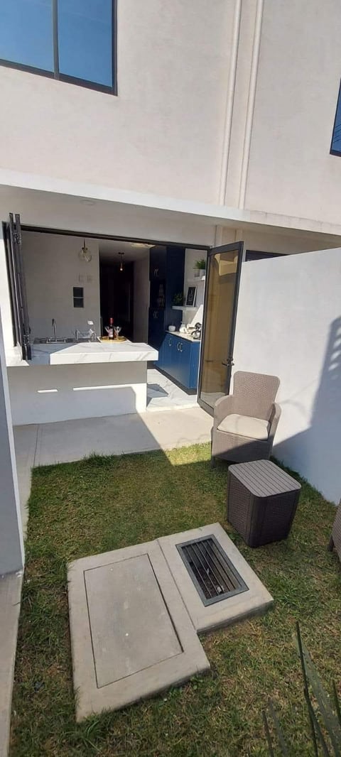 Modern patio with synthetic grass, white kitchen counter, rattan furniture, and open doorway leading to interior room with blue cabinetry