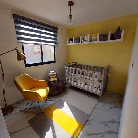 Modern baby nursery with yellow walls, white crib, yellow chair, striped roman blind, and pendant light